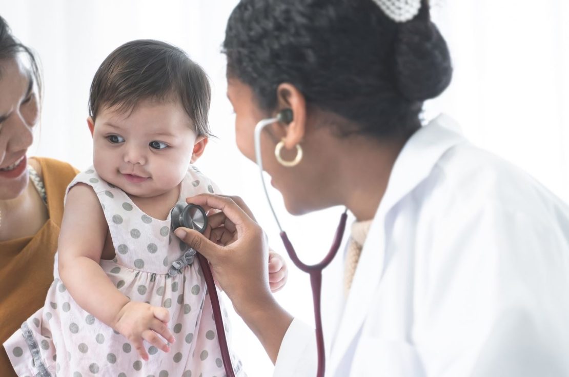 A new mother takes her baby to the doctor who is listening to the child's heartrate with a stethoscope