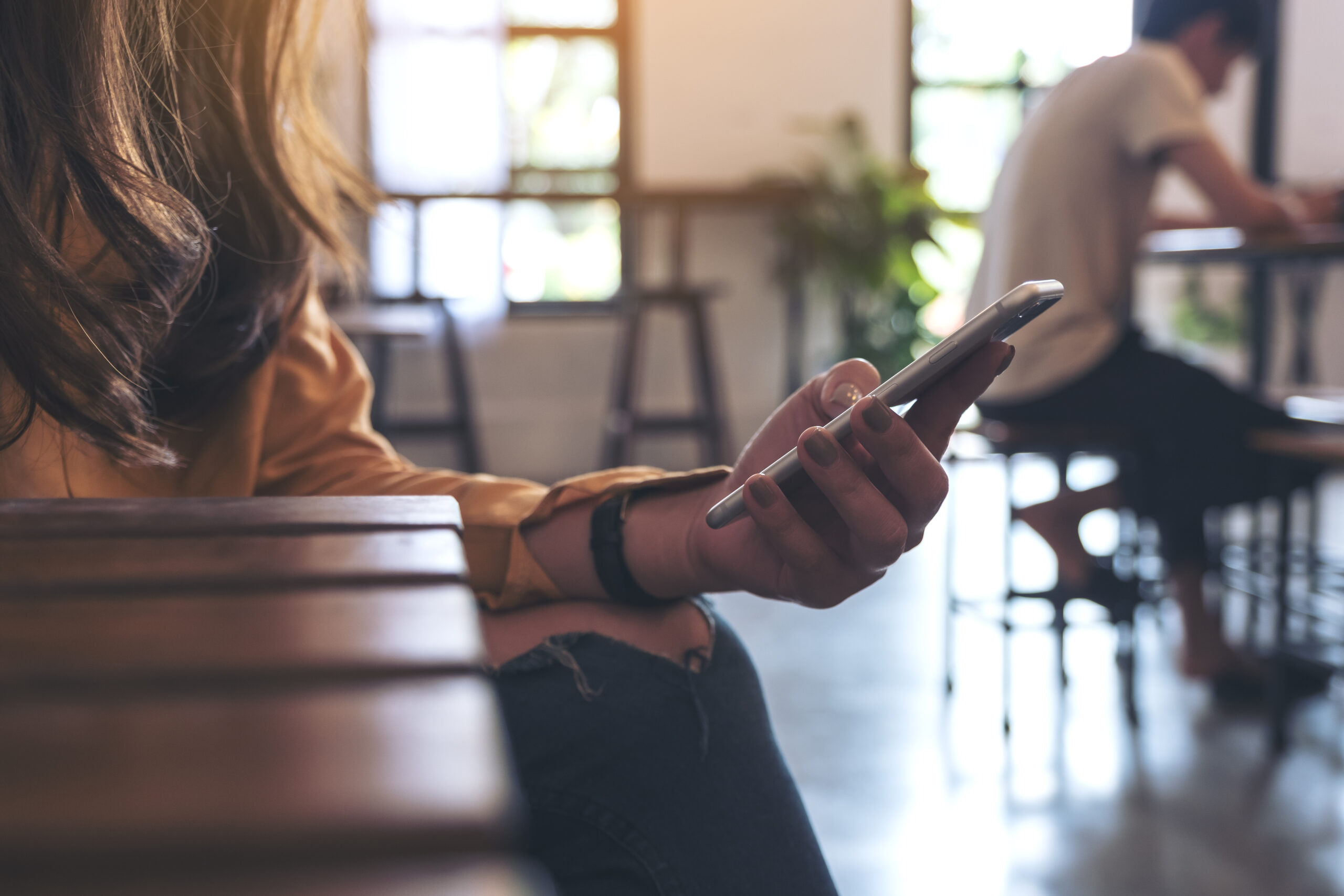 Closeup image of a woman holding , using and looking at smart phone in cafe
