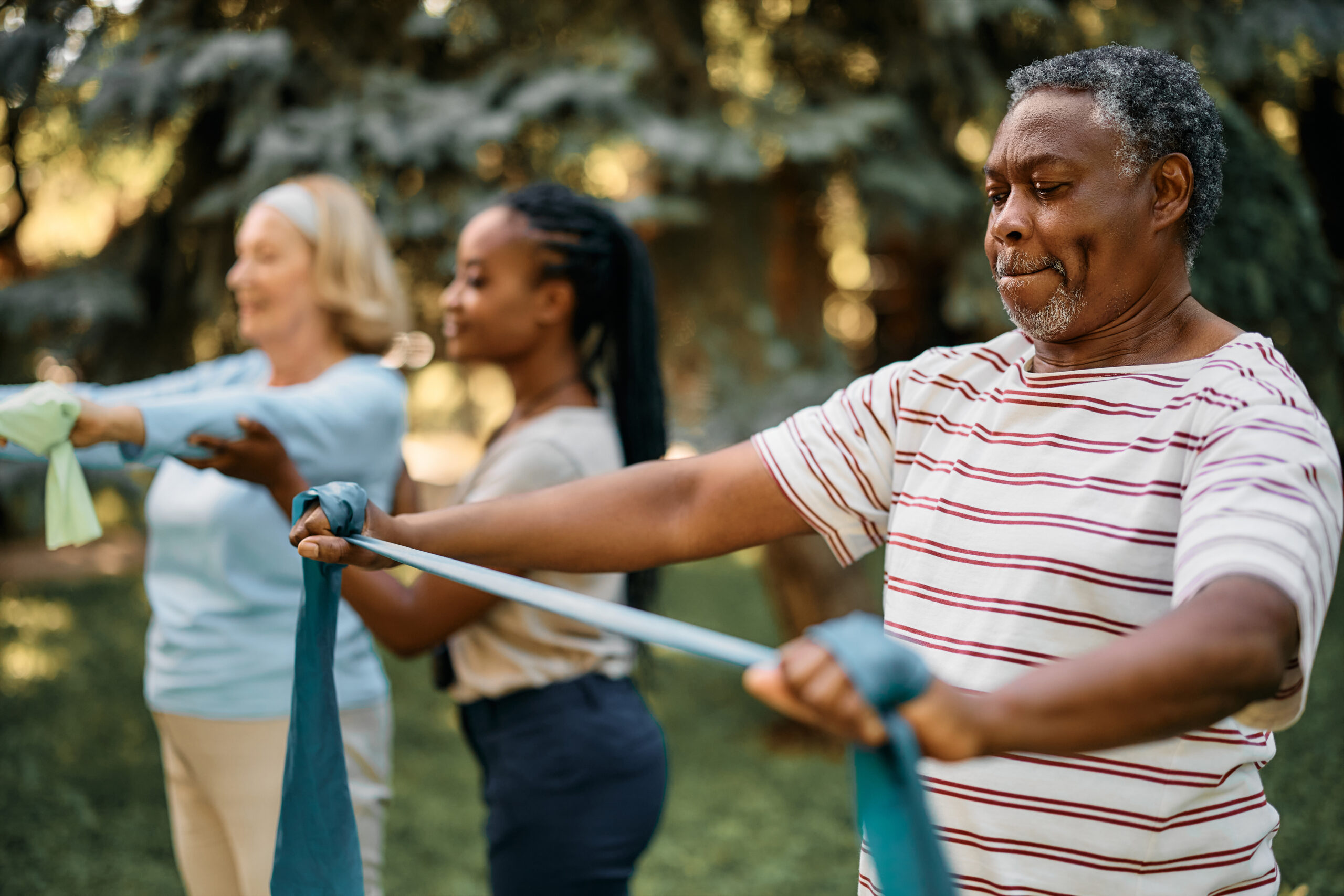 A couple of older people take part in an outdoor exercise class using physio bands