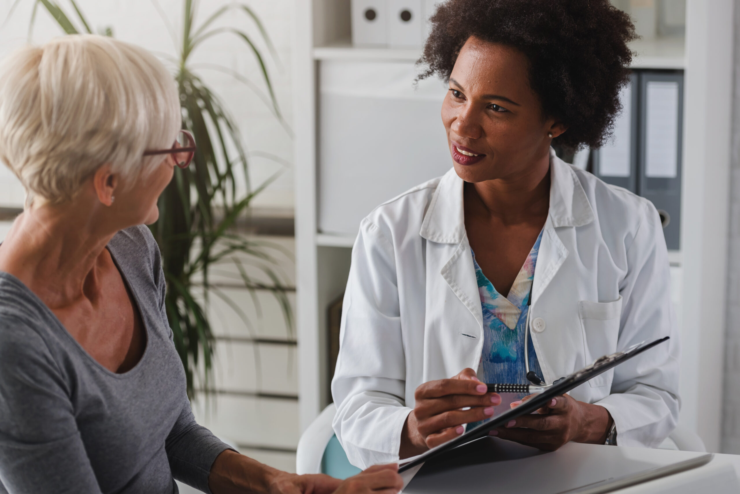 A doctor sits at her desk and chats to an older woman
