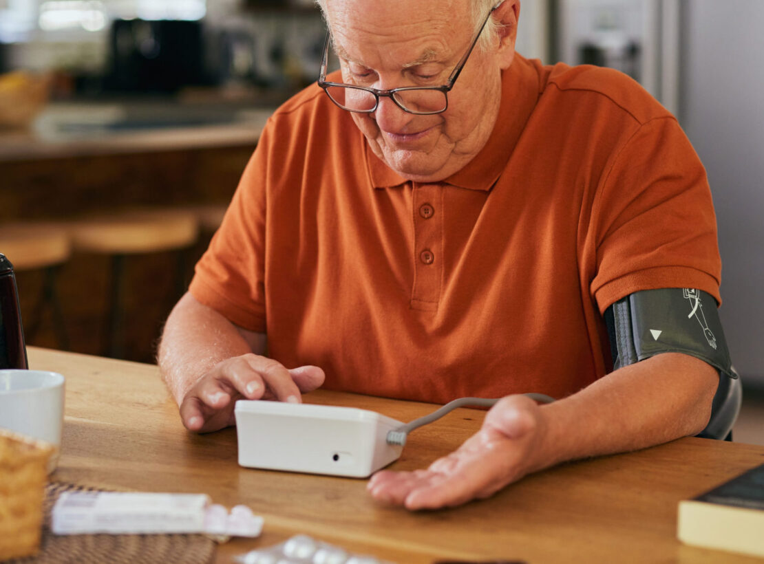 Older man checking his blood pressure at home with a digital device.