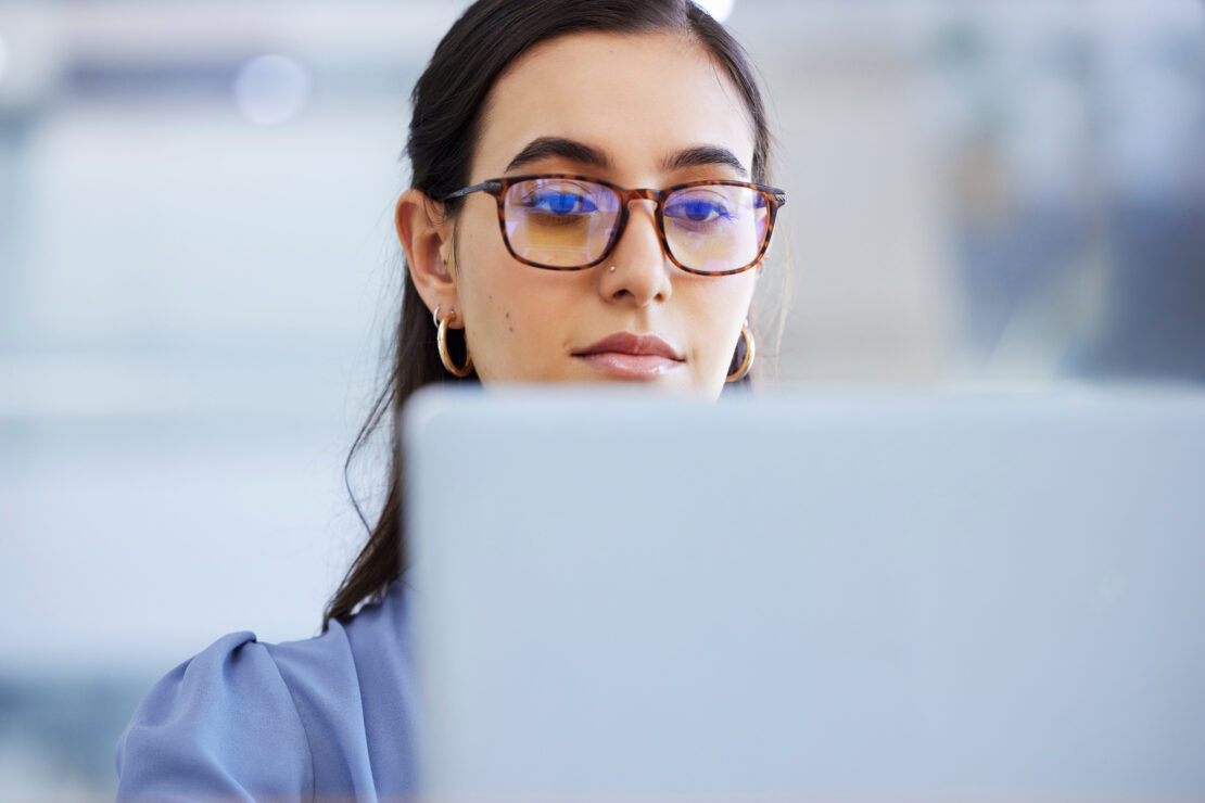 Business woman, glasses and working on laptop in office, agency and startup company. Focus, face and female worker on computer technology for email, internet planning and professional seo research.