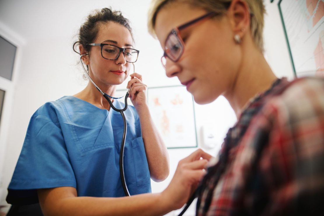 Nurse listens to patient's heart through stethoscope