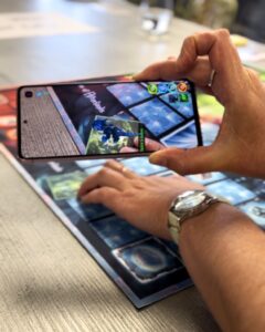 Someone holds a phone screen over a board game, displaying an animated dragon