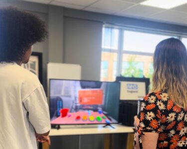 Two people watch a screen displaying a virtual waiting room game for young children in hospital