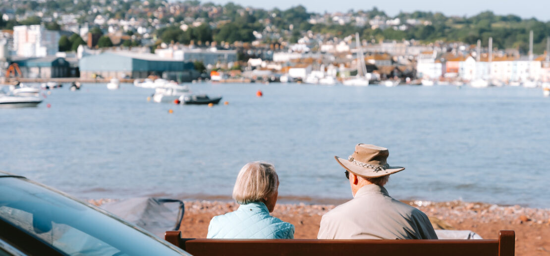 Older couple sitting on bench looking out over a cornish seaside view